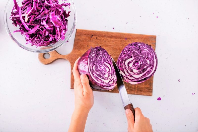 person cutting red cabbage on a cutting board