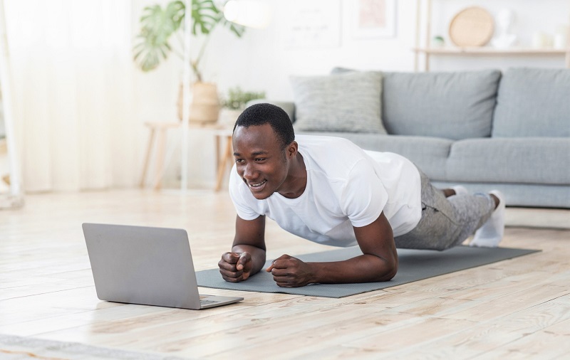 a man doing a home workout on a yoga mat while looking at his computer. holiday gift ideas