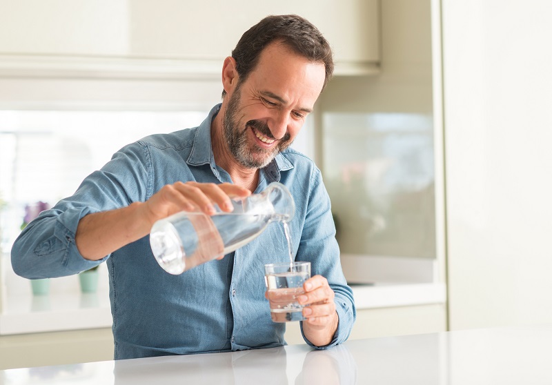 a smiling man pouring water into a glass