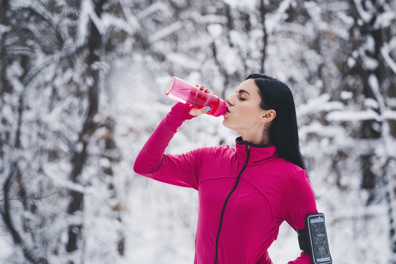 a woman taking a water brake while on a winter run. winter weight loss tips