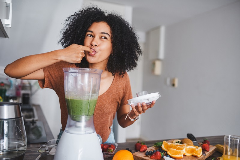 a woman tasting a fruit smoothie from a blender. holiday gift ideas
