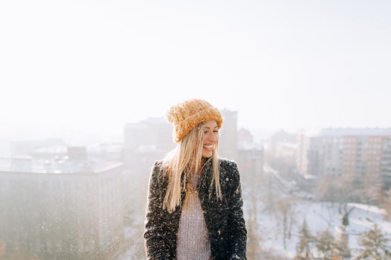 a smiling woman standing on a rooftop while it snows. winter weight loss tips