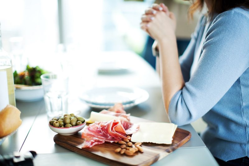a woman sitting in front of a platter of cured meats, olives, and cheeses. healthy snack ideas