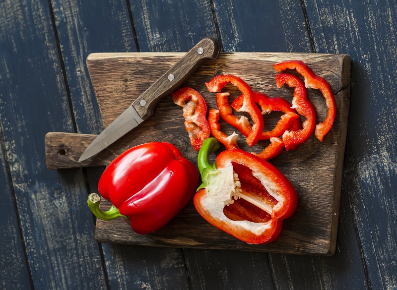 two red bell peppers on a wooden cutting board