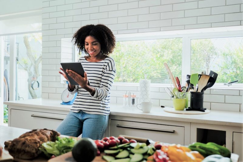 woman looking at tablet in kitchen while making DIY meals