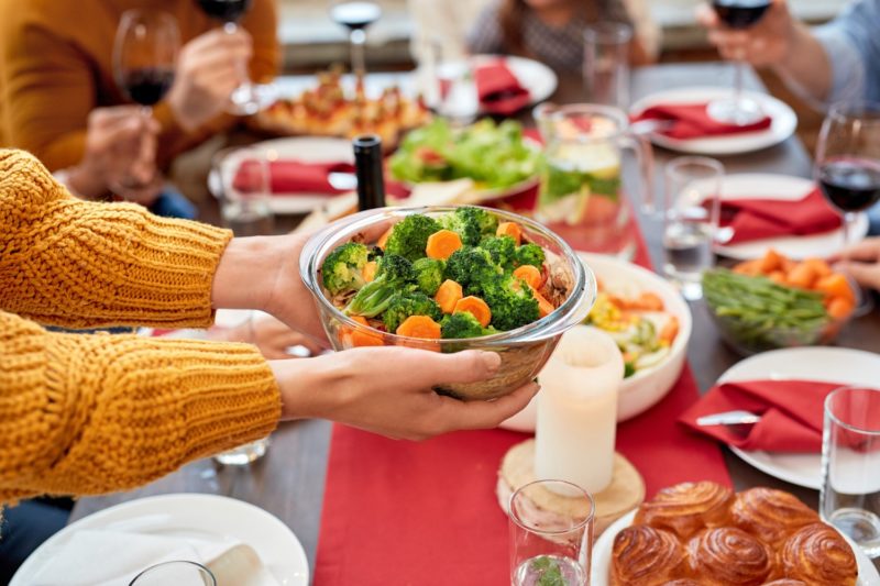 Woman holding bowl full vegetables over served holiday dinner table